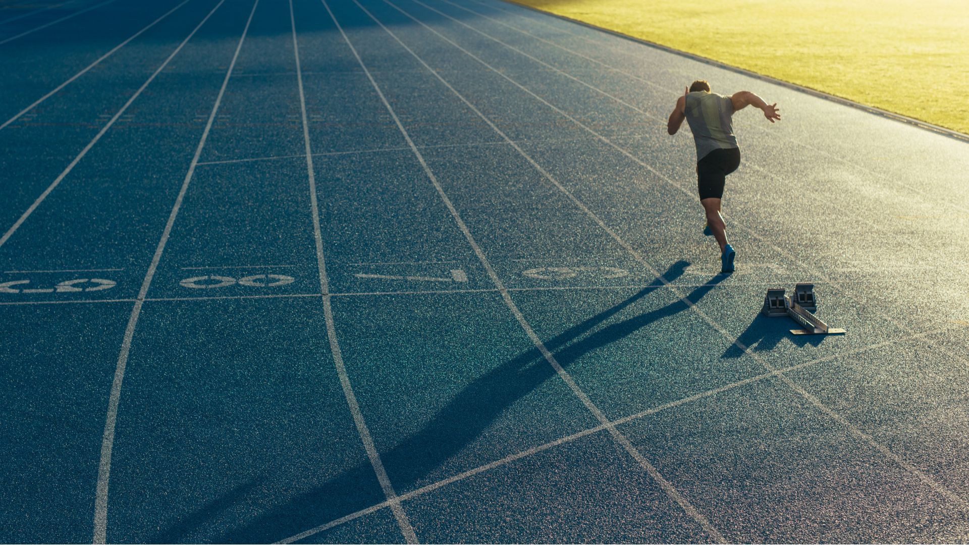 A man sprinting on a track, with a distinct shadow cast beside him, illustrating motion and determination.