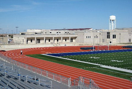 A football field featuring bleachers and a prominent water tower in the background, showcasing a vibrant sports environment